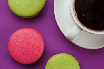 Glass of coffee top view with pink and green cookies on a purple background.