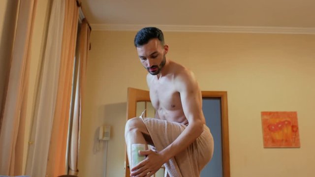 A young guy with a beard makes wax legs. A man pulls a strip for depilation and falls on the bed in pain. 4k. 4k video