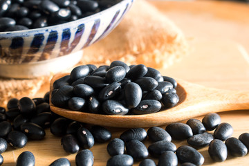 Raw black beans in wooden spoon on table.