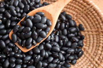 Raw black beans in basket and spoon on wood table.
