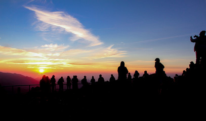 Colorful sunrise with the silhouettes of many people on top of a mountain in Flores, south-east Asia.