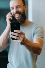 Networking obsession. Bearded hipster guy checking social media feed while having phone conversation, smiling.