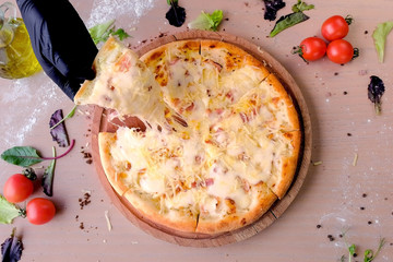 Cook takes a slice of pizza with a gloved hand. Hand close-up