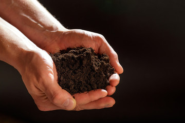 Soil in male hands on dark background ..