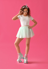 Beautiful young woman on roller skates against color background
