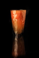 raw carrot juice in tall faceted plastic glass with reflection