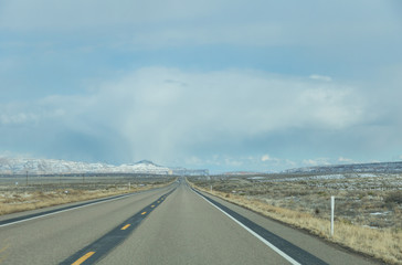 Fototapeta premium Straight road ahead with overcast sky above snowcapped mountain in Utah, USA