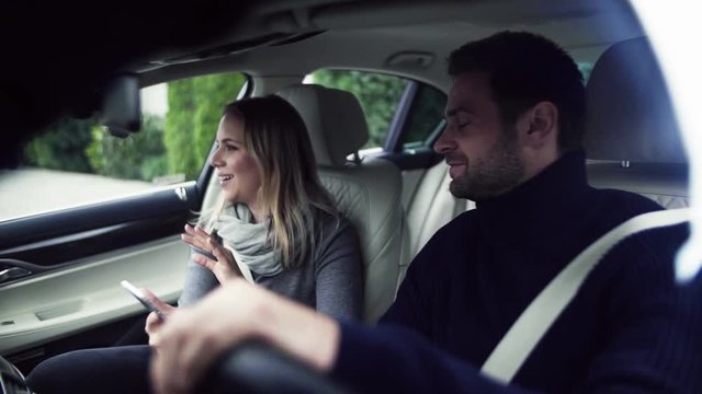Happy young couple with smartphone sitting in car, talking. Slow motion.