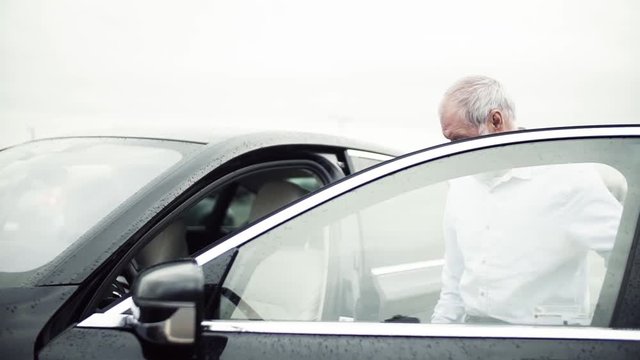 Senior man getting in car, rainy weather.
