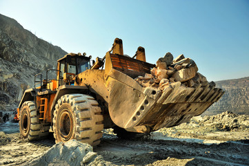Wheel loader machine unloading rocks in the open-mine of iron ore
