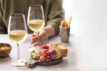 Woman holding glass of white wine in the restaurant. Different snacks, Blue cheese, olives, baguette slices and cured meat. Tasting party lifestylebackground.