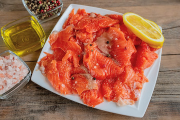 Raw pickled trout fillet and salmon pieces in a white plate. Wooden background. The view from the top. Healthy tasty food