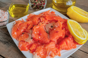 Raw pickled trout fillet and salmon pieces in a white plate. Wooden background. The view from the top. Healthy tasty food