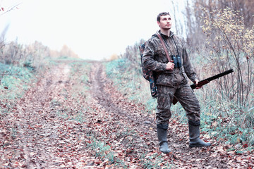 A man in camouflage and with a hunting rifle in a forest on a spring hunt