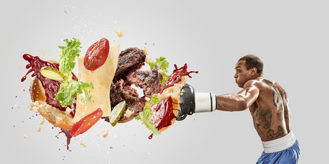 Fight the fast food. Burger's crashing by the boxer isolated on white background. Combination of...