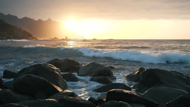 Ocean waves crash on rocks and spray in beautiful sunset light at Benijo beach in Tenerife, Canary Islands