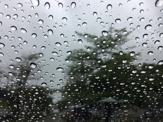 The raindrops on the windscreen or windshield or car glass. View from the inside of the car with a grey sky background