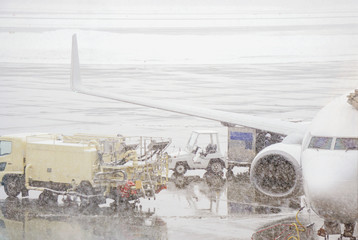 Naklejka na ściany i meble White airplane parked and fuel truck prepare to refuel on ground with heavy cotton snowing in the airport.