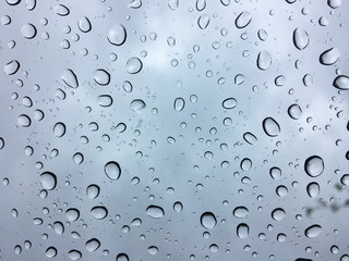 The raindrops on the windscreen or windshield or car glass. View from the inside of the car with a grey sky background