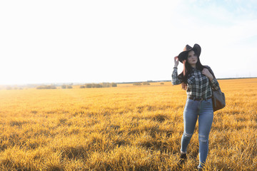 A young girl is traveling around the city hitchhiking. A beautiful young girl went on vacation. A female student in a cowboy hat on the road in autumn.