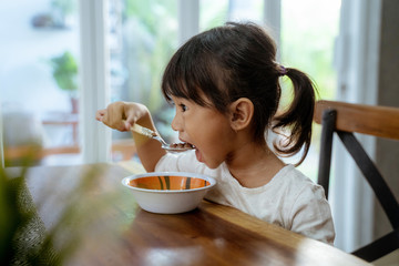 asian beautiful toddler girl having breakfast by herself in the morning at dining room