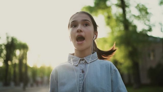 Happy child, teenager walks on the sidewalk, listening to music and sings a song. Good sunny day. Positive mood life is good. 4K