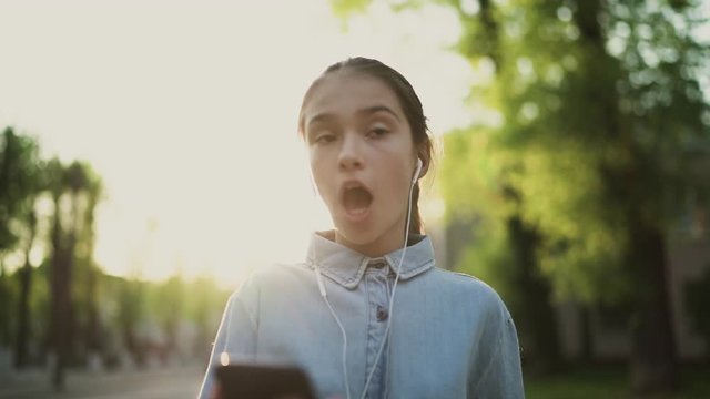 Happy child, teenager walks on the sidewalk, listening to music and sings a song. Good sunny day. Positive mood life is good. Slow motion 100 fps