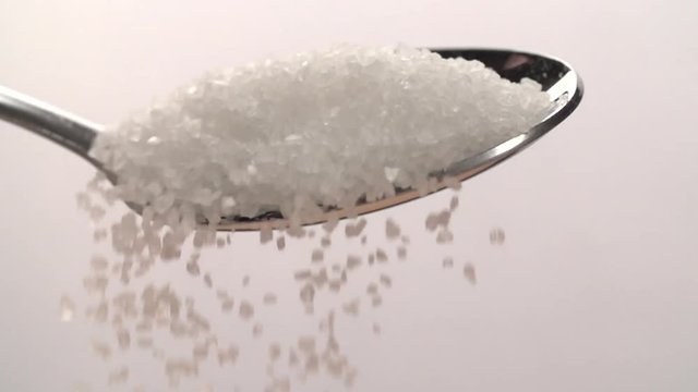 Sugar is pouring Slow motion from teaspoon on white Background