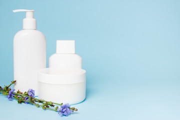 White jars of cosmetics with flowers on a blue background. Bath accessories. Face and body care concept.