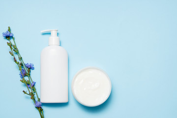 White jars of cosmetics with flowers on a blue background. Bath accessories. Face and body care concept. Top view