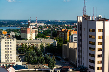 Obraz premium Voronezh, Russia, June 11, 2019: View from window of skyscraper on modern high-rise buildings on right bank of river. In background is bridge over Vornezh River and pipes of thermal power station.