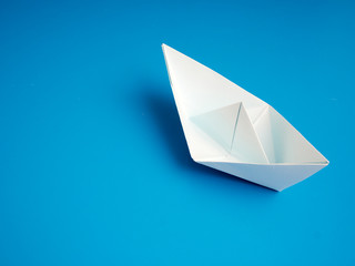 Single white paper boat on a blue background