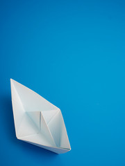 Single white paper boat on a blue background