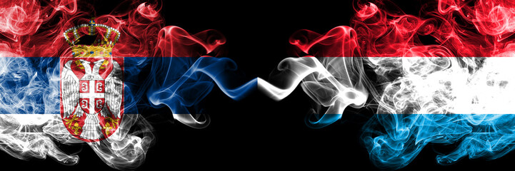 Serbia vs Luxembourg smoky mystic flags placed side by side. Thick colored silky smokes combination of Serbian and Luxembourg flag