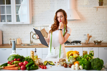 Young beautiful woman using tablet while cooking in the modern kitchen. Healthy eating, vitamins, dieting, technology and people concept. Losing Weight