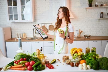Young beautiful woman using tablet with infographic while cooking in the modern kitchen. Healthy eating, vitamins, dieting, technology and people concept. Losing Weight
