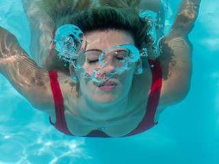 Fototapeta premium Blonde girl diving in the pool and breathing out air to make bubbles.