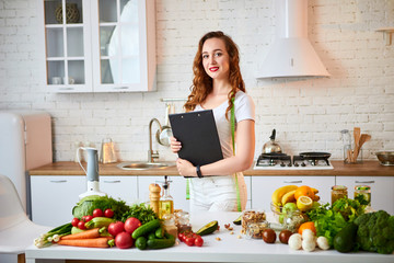 Young beautiful woman using tablet while cooking in the modern kitchen. Healthy eating, vitamins, dieting, technology and people concept. Losing Weight