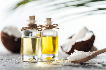 selective focus of bottles with coconut oil near cracked coconuts and wooden spoon with coconut shavings