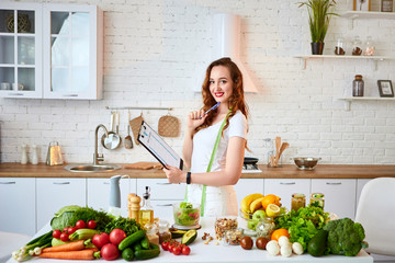 Young beautiful woman using tablet with infographic while cooking in the modern kitchen. Healthy eating, vitamins, dieting, technology and people concept. Losing Weight