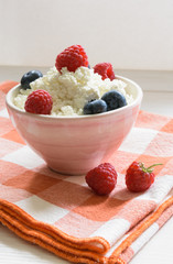 bowl of cottage cheese with raspberries and blueberriesand on the red plaid litter on a white wooden table