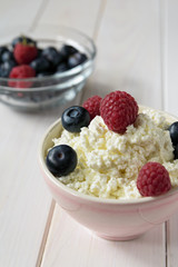 bowl with cottage cheese, raspberries and blueberries on a light wooden table