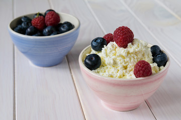 bowl with cottage cheese, raspberries and blueberries on a light wooden table