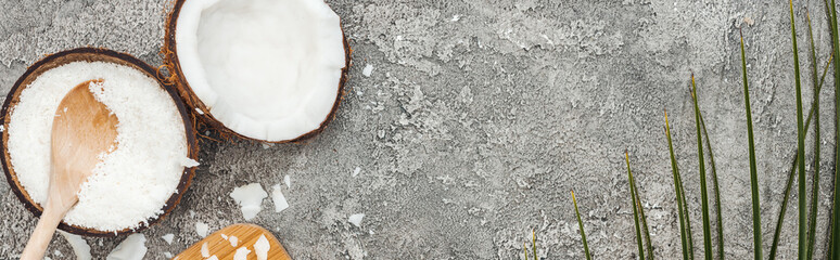 top view of coconut halves and flakes on grey textured background with copy space, panoramic shot