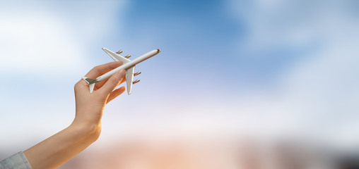 Hand holding a plane over blurred city background with sky.Tourism or travel concept