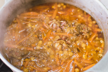 Cooking oriental pilaf in the kitchen in the cauldron. A woman prepares a dish of lamb, beef, rice, chickpeas, carrots