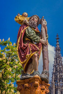 Statue of St. Christopher on top of the Christophorus fountain (Christophorusbrunnen) with the tower of the Ulm Minster in the background in Ulm, Germany