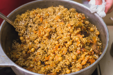 Cooking oriental pilaf in the kitchen in the cauldron. A woman prepares a dish of lamb, beef, rice, chickpeas, carrots