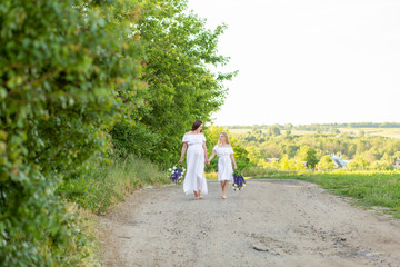 Mom and daughter with long hair with a bouquet in their hands. Family walking in the countryside outside the city