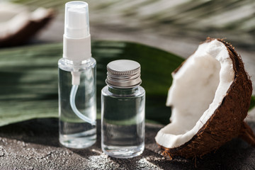 selective focus of bottles with coconut water near coconut half and palm leaf on grey textured background
